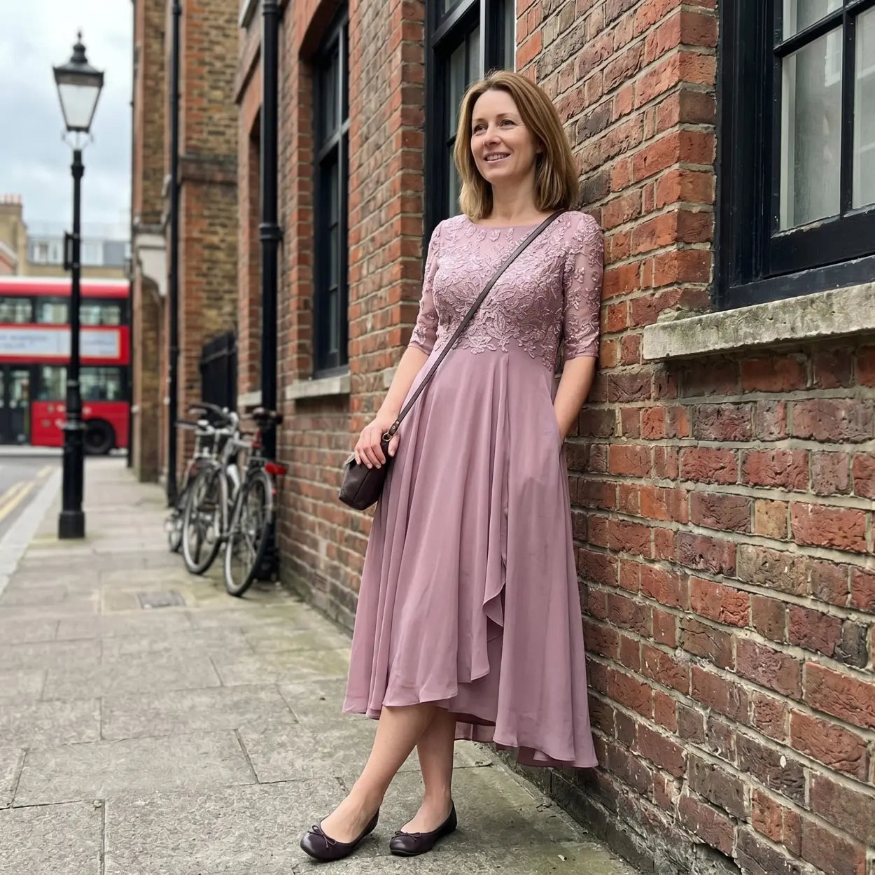 Woman in a pink dress leaning against a brick wall on a city street.