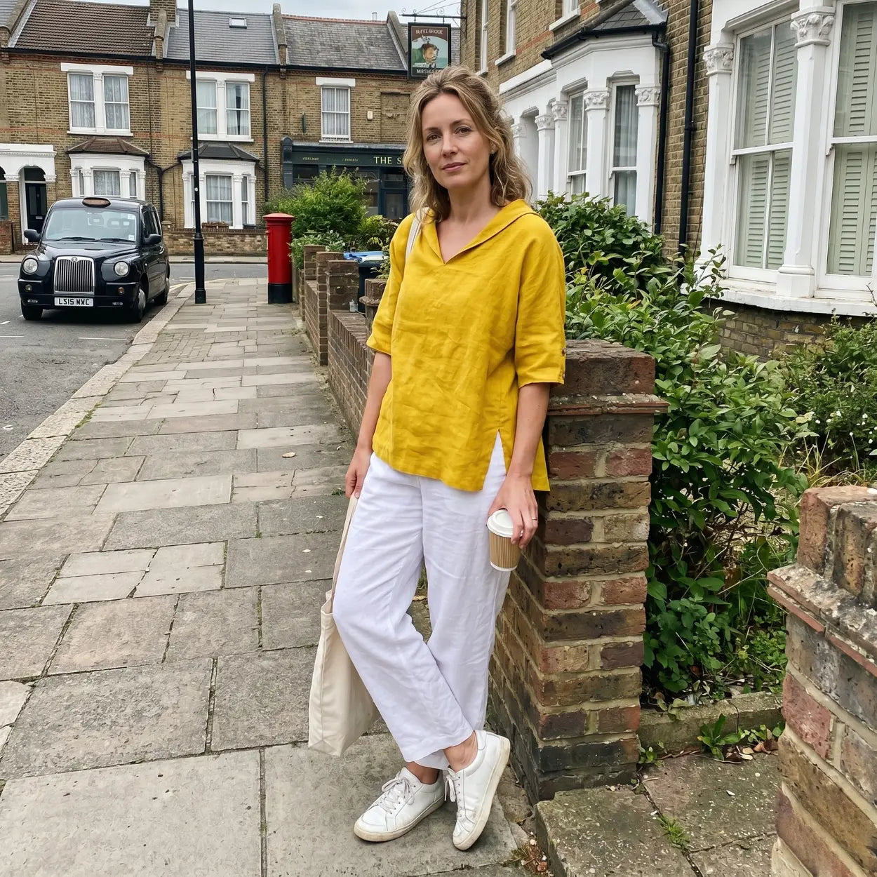 Woman in a yellow top and white pants standing on a street with a taxi in the background